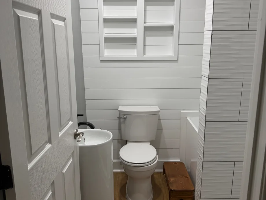 Remodeled bathroom with a white textured tile wall, toilet and wood floor